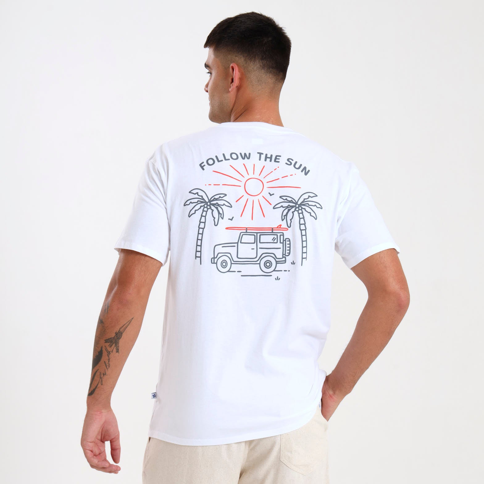 A man wearing a white crew neck t-shirt with a graphic print on the back, featuring a jeep and text saying "Follow the sun".