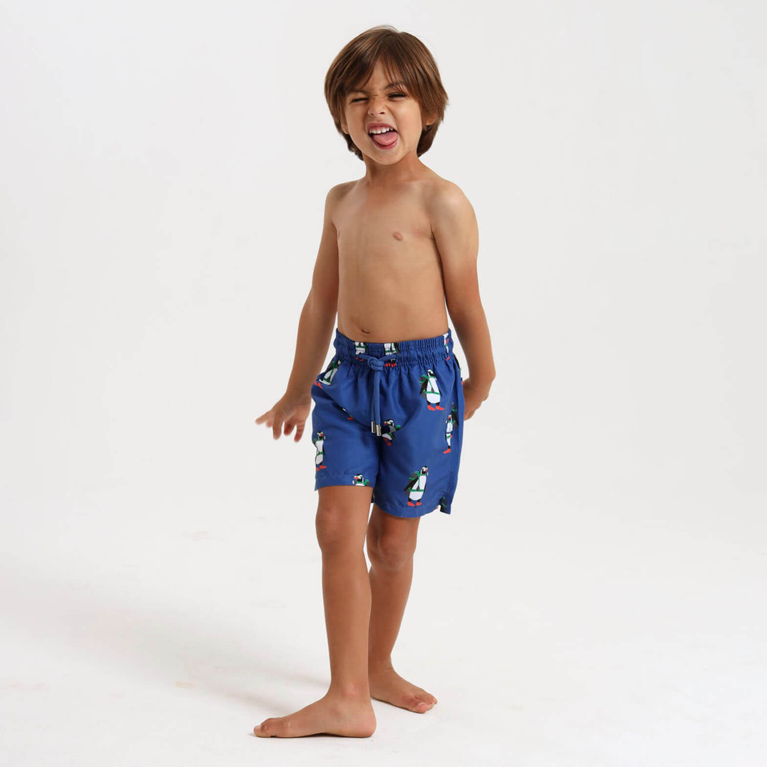 Young boy wearing royal blue swim shorts with a scuba penguin pattern all over.