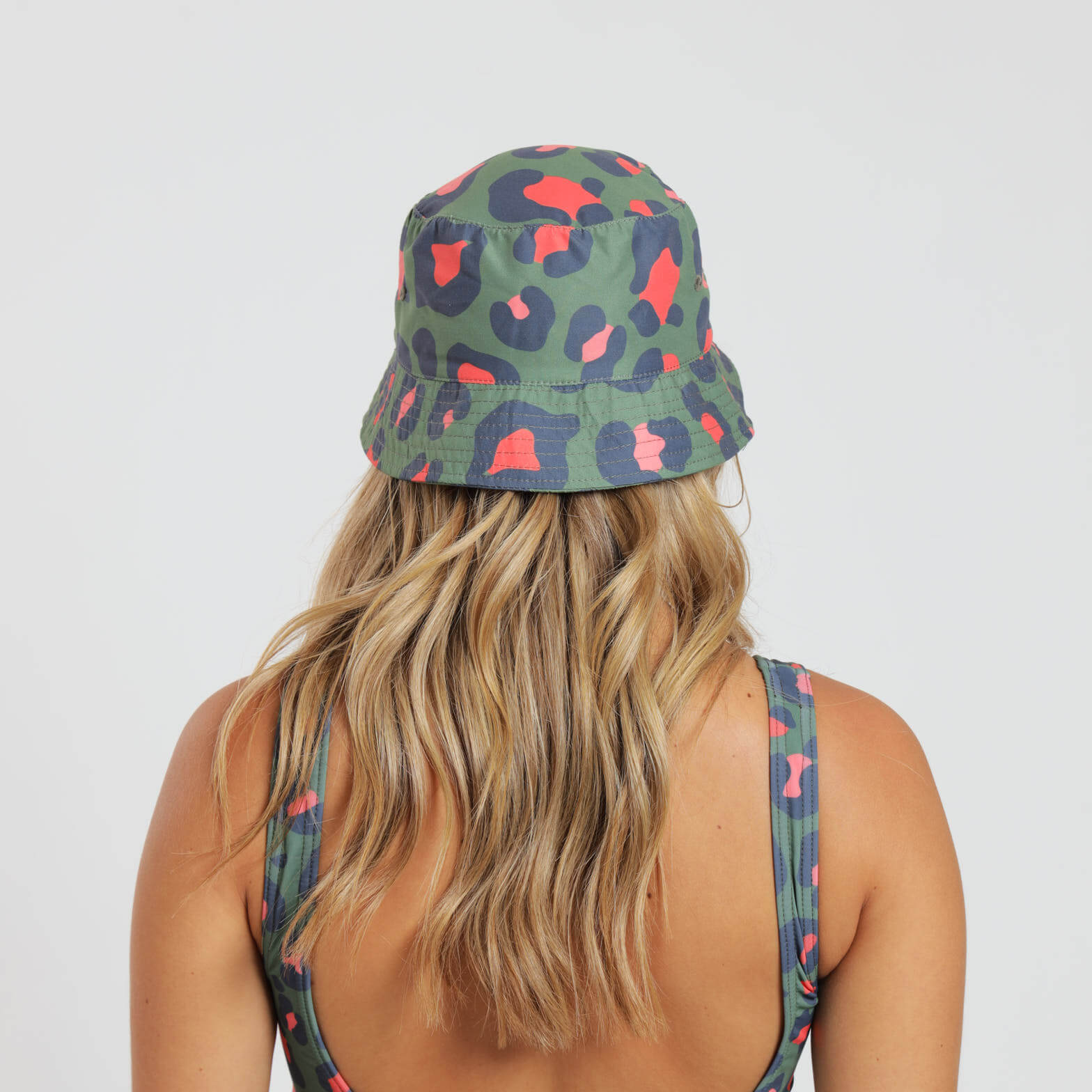 A woman wearing an army green and orange bucket hat which features and all over leopard print design.
