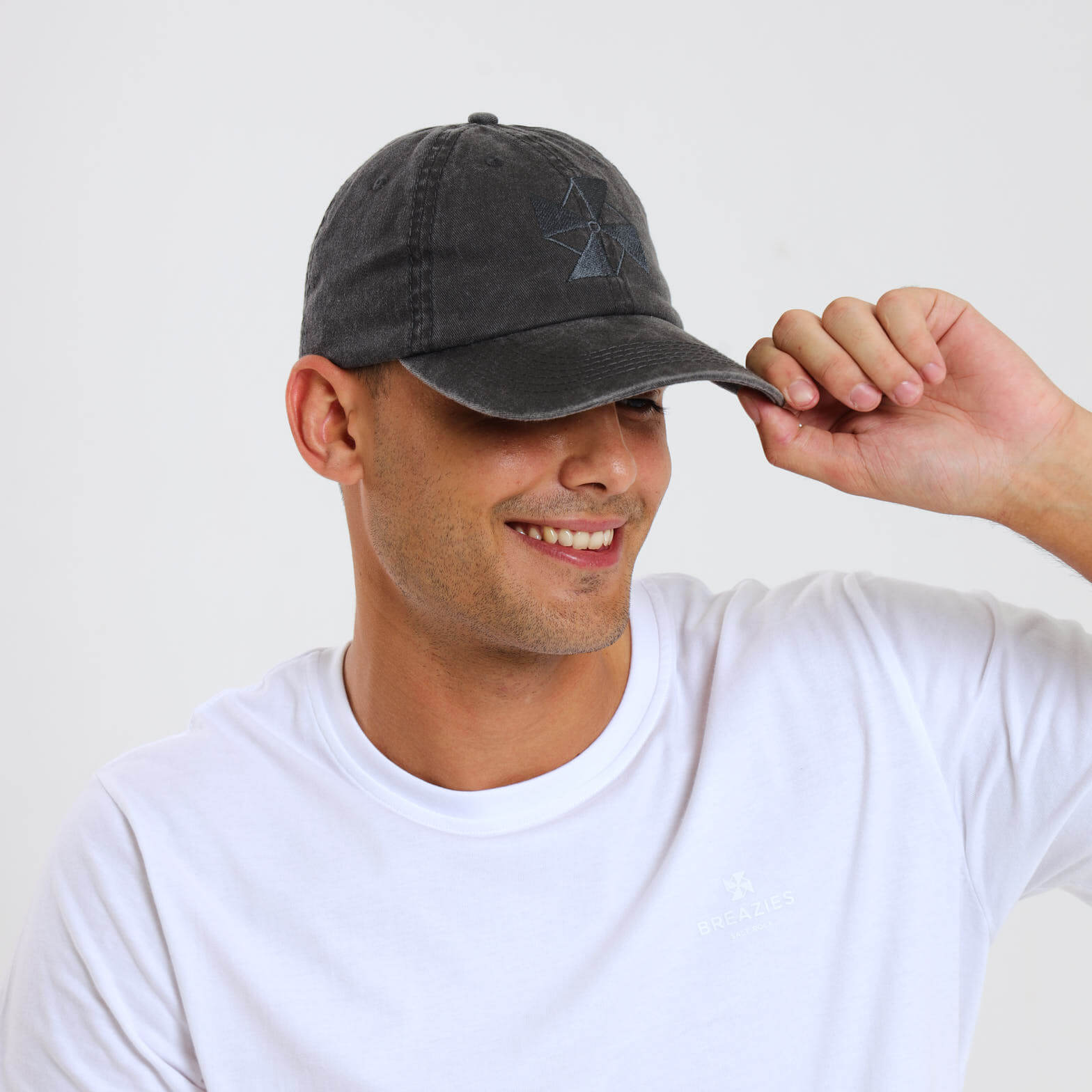 A male model wearing a black material cap featuring a subtle embroidered Breazies logo on the front panel.