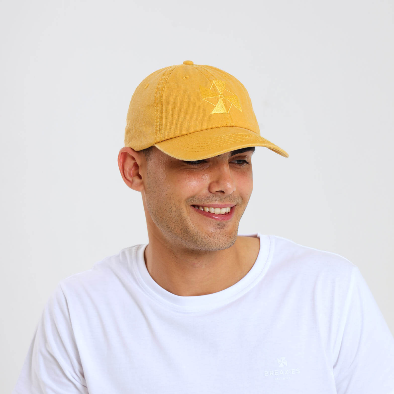 A male model wearing a yellow cap featuring a subtle embroidered Breazies logo on the front panel.