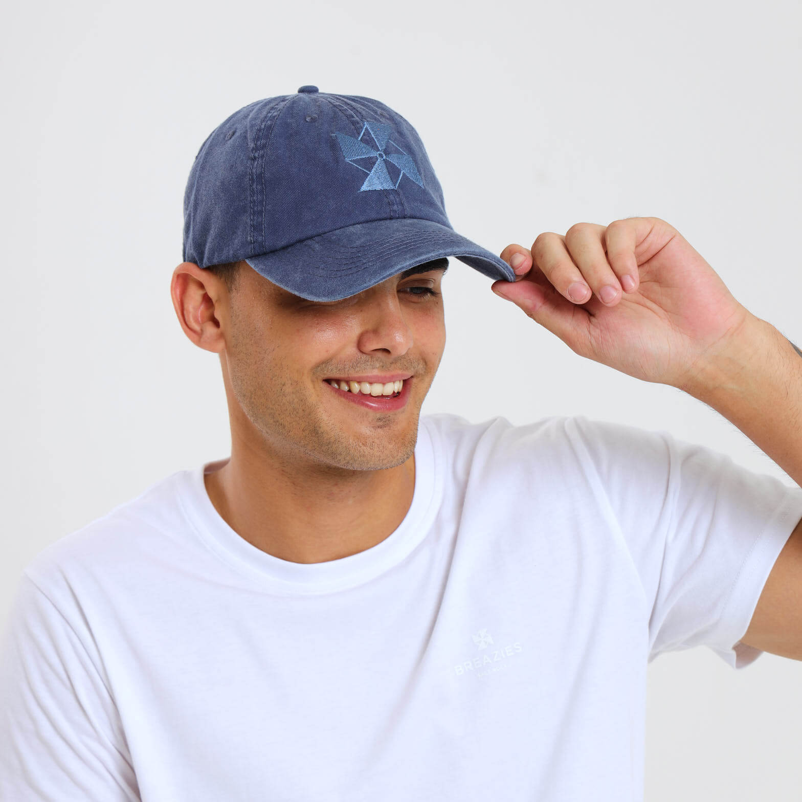 A man wearing a navy blue cap made from washed twill featuring a subtle embroidered Breazies logo on the front panel.