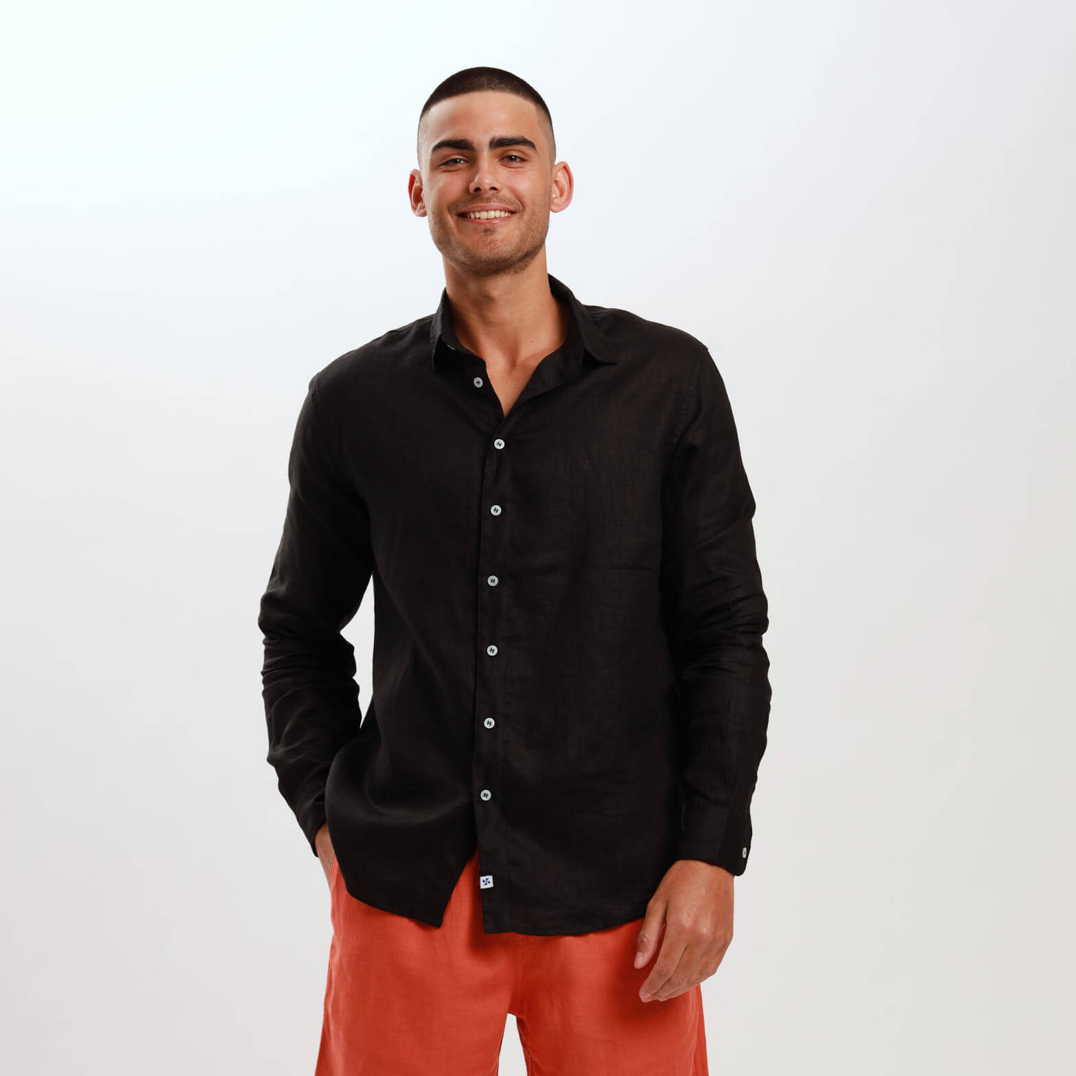 A man wearing a long sleeve black linen shirt with the collar visible and buttoned up to the neck.