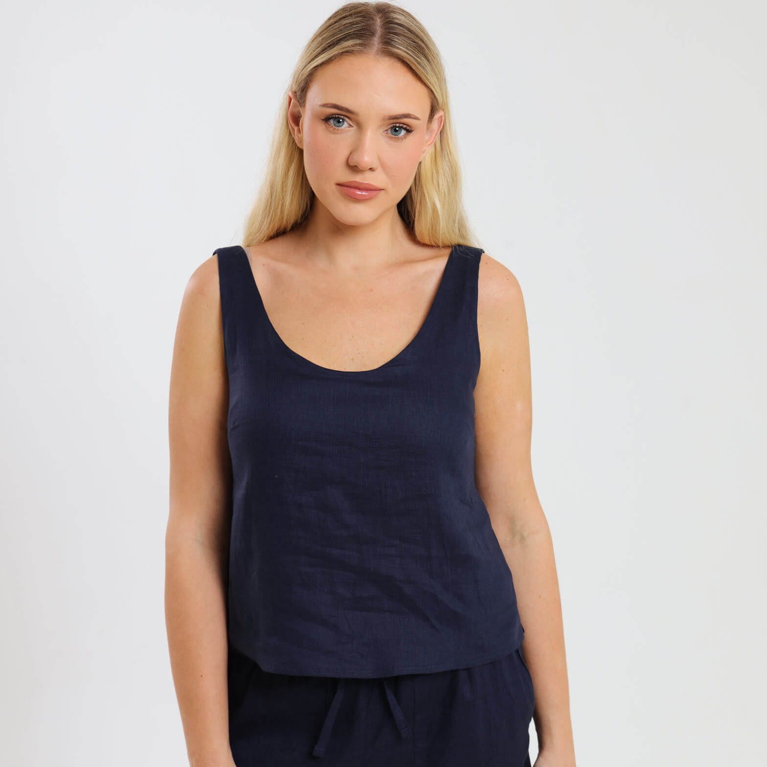A navy blue sleeveless camisole top with a gentle V-neckline, worn by a model with matching navy linen shorts.