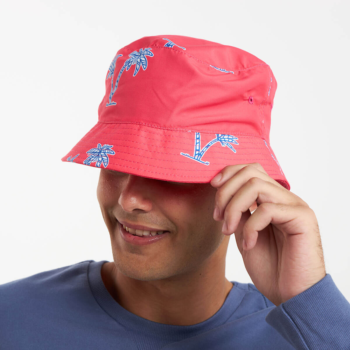 A man wearing a coral red bucket hat that features a blue palm print.