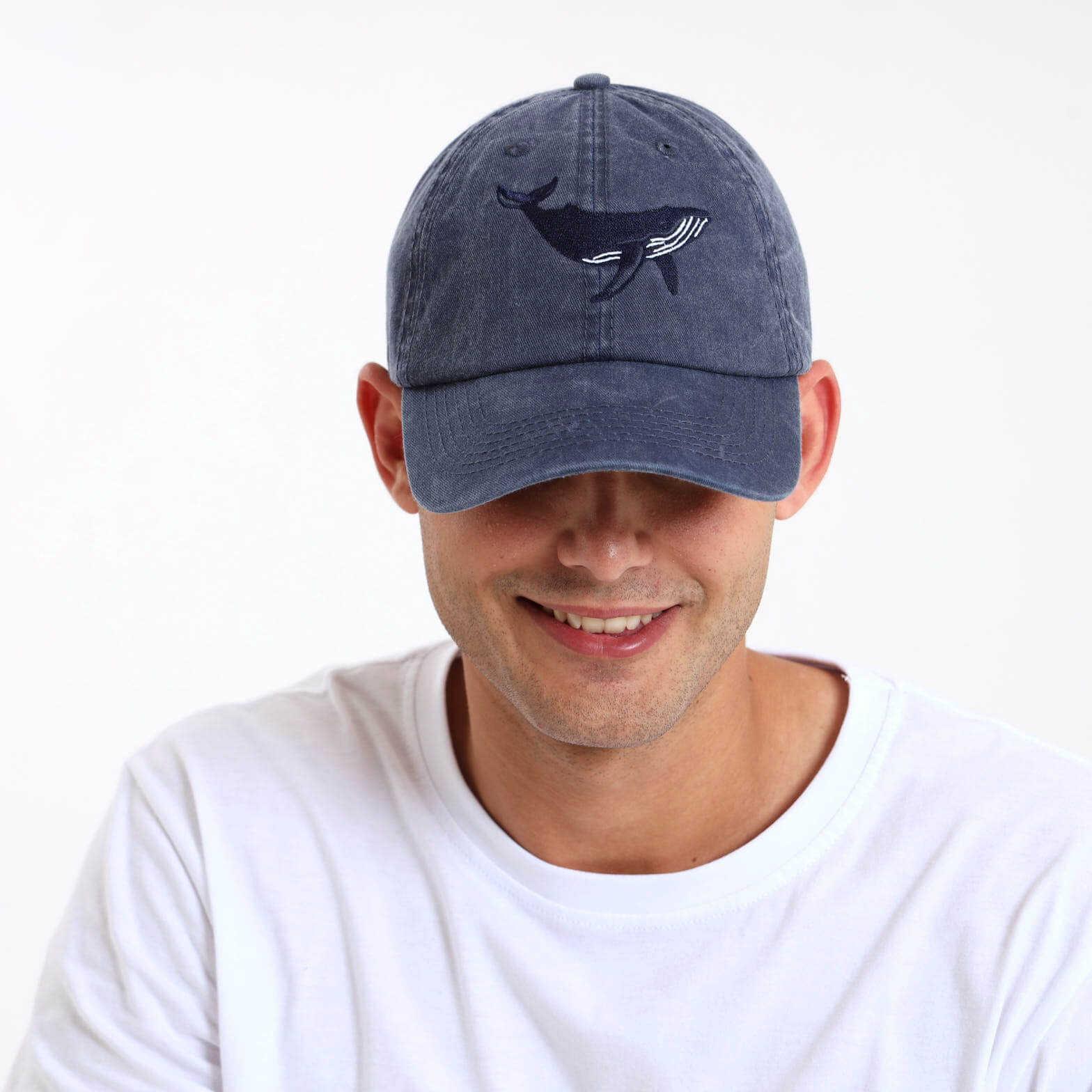 Man wearing a navy blue cap with an embroidered whale on the front.