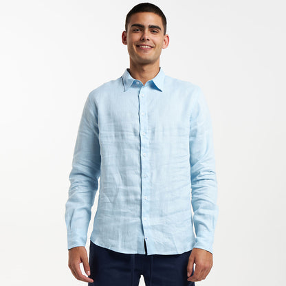 A man wearing a long sleeve baby blue linen shirt with the collar visible and buttoned up to the neck.
