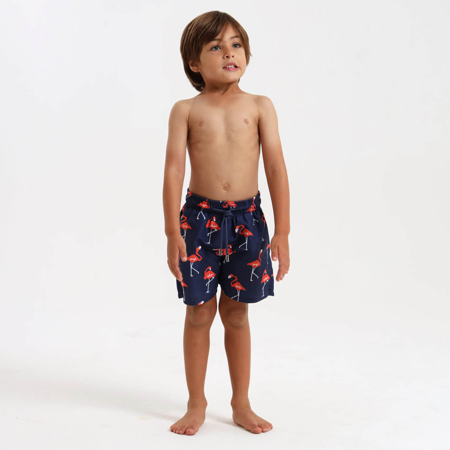 Young boy wearing navy swim shorts with an orange flamingo pattern.