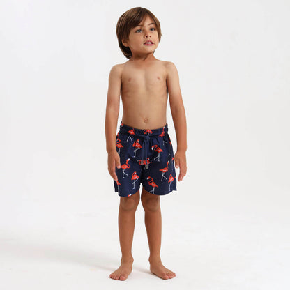 Young boy wearing navy swim shorts with an orange flamingo pattern.