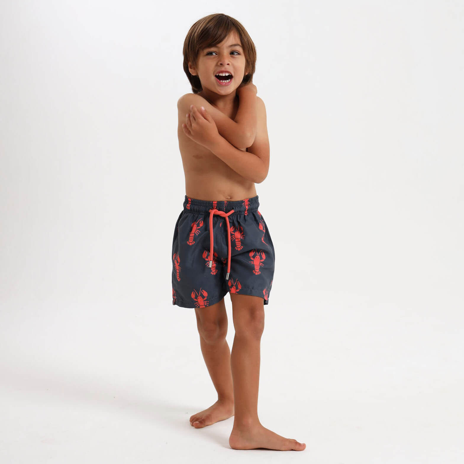 Boy wearing swim shorts with an adjustable waist band and a quirky lobster design.