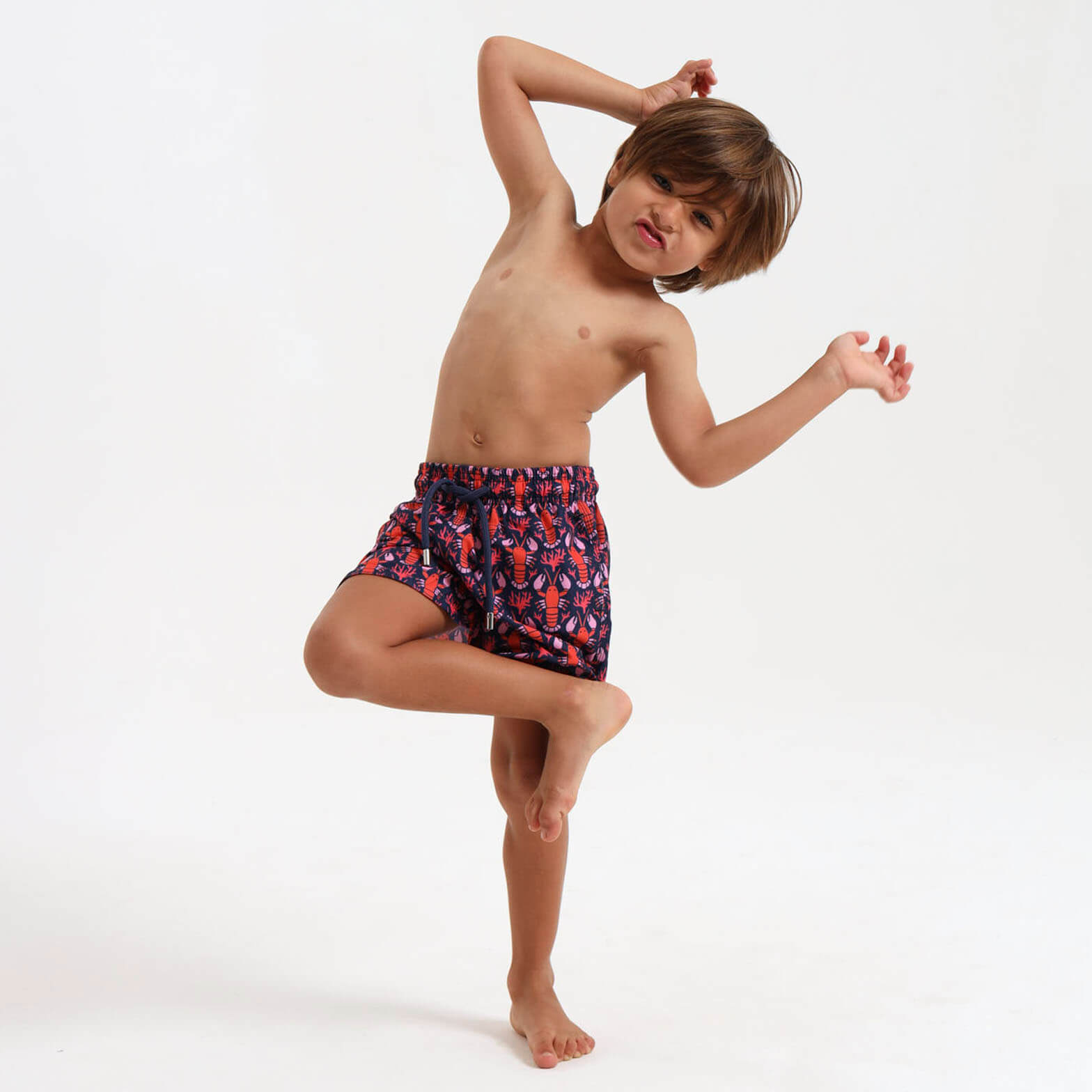 Boy wearing navy swim shorts with an  orange lobster design.