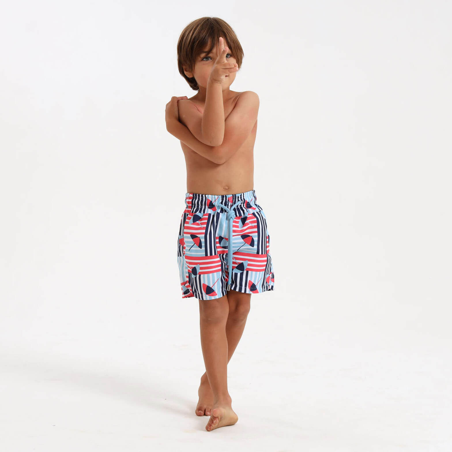 Boy wearing fun swim shorts with a blue umbrella print.