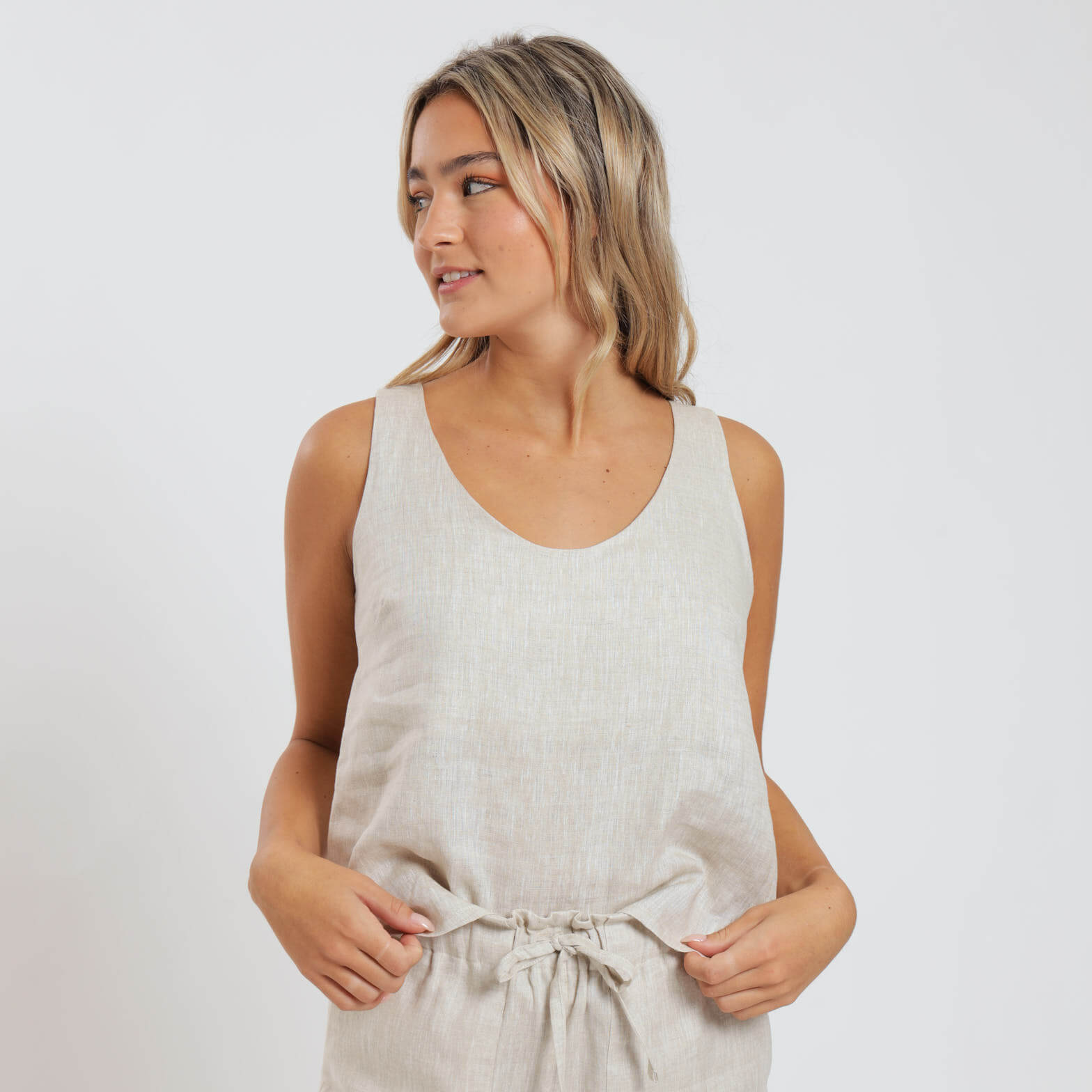 A woman wearing a beige sleeveless linen cami top with a round neck and elegant shoulder straps.