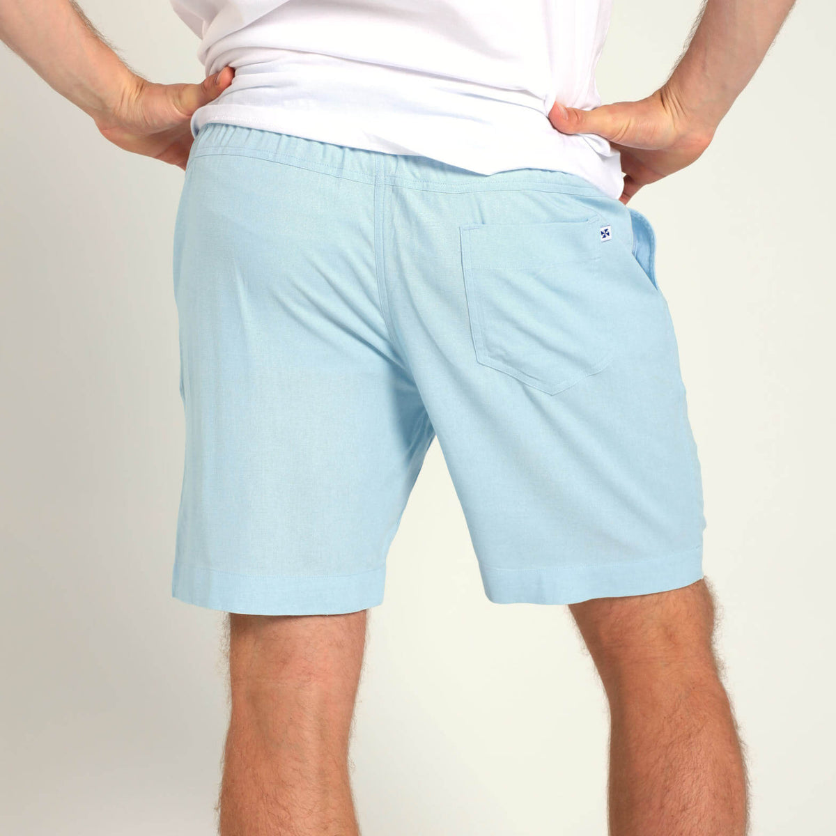 A man wearing Breazies light blue casual shorts and a white t-shirt, shown from the back against a plain light background.
