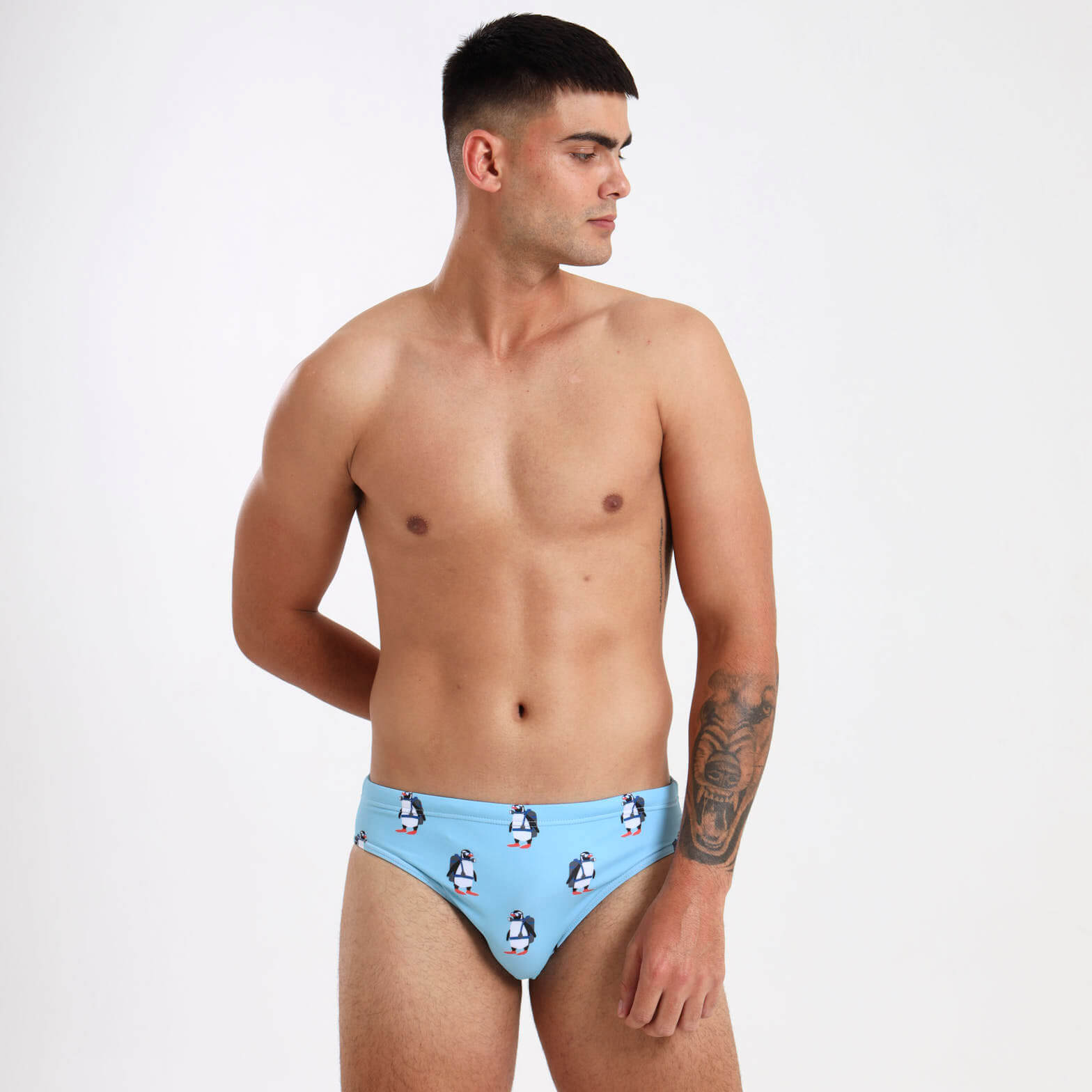Man wearing light blue swim briefs with a quirky penguin pattern on them.