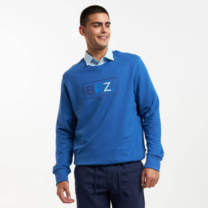 A man wearing a royal blue crew neck sweater with a flat printed logo on the chest, elasticated neck, cuffs, and hem.