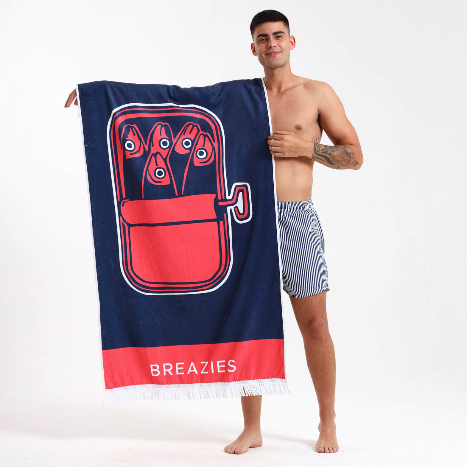 Man holding a navy beach towel with a sardine illustration and Breazies banding on it.