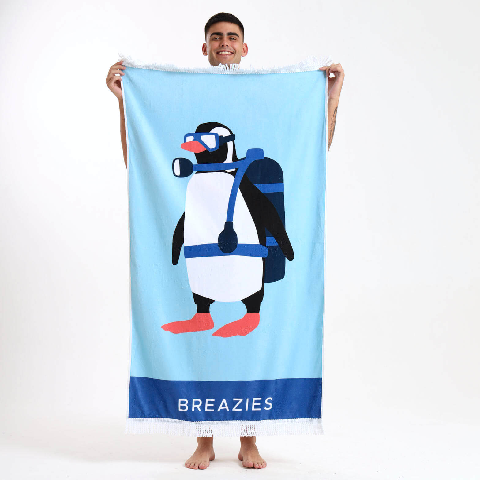 Person holding a light blue beach towel with a penguin design and 'Breazies' branding.