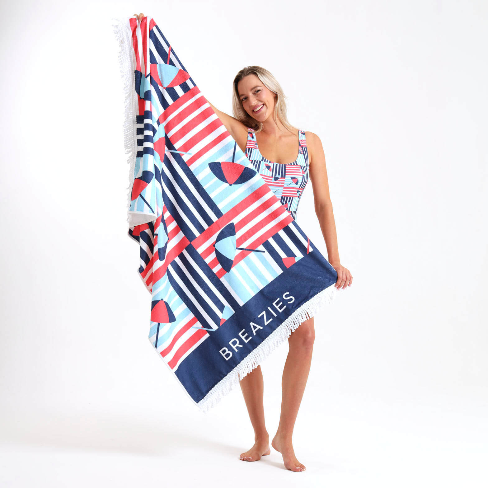 Woman holding a colourfully striped beach towel with 'Breazies' branding.