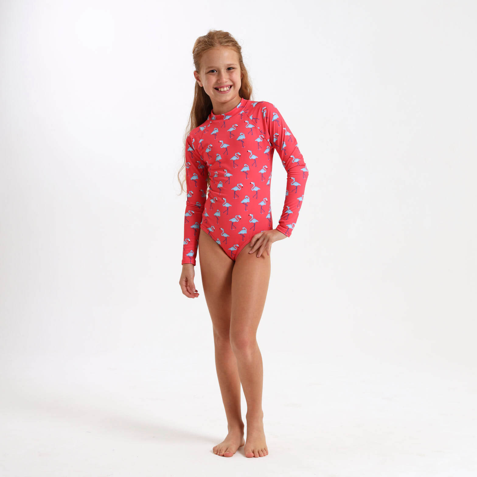 Young girl wearing a long sleeve swimsuit with a coral and blue flamingo print on it.