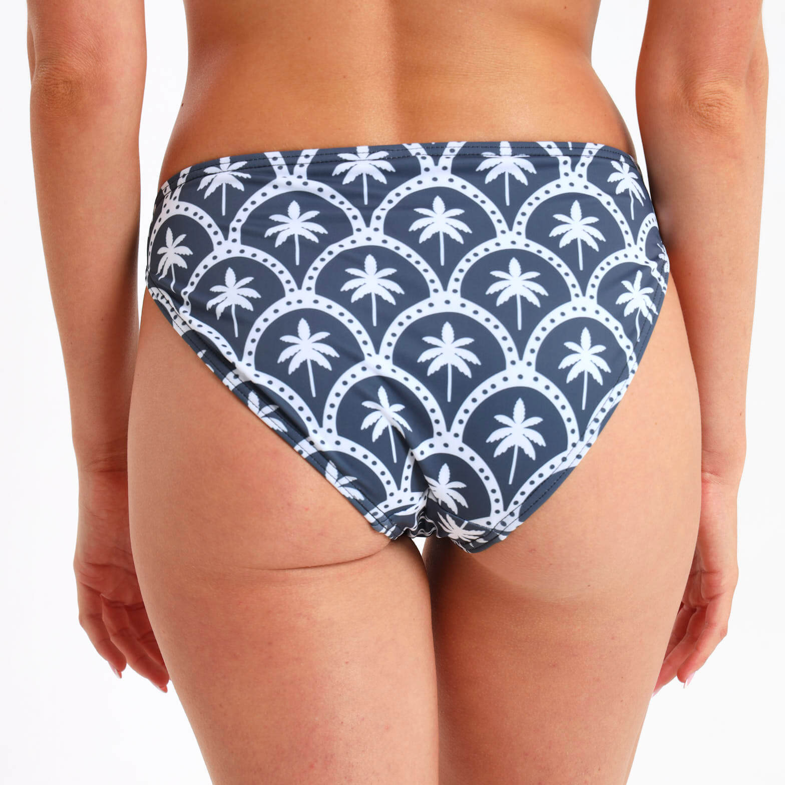 Steel blue bikini bottom with a slightly cheeky bum and an all over white palm print  being worn by a woman.